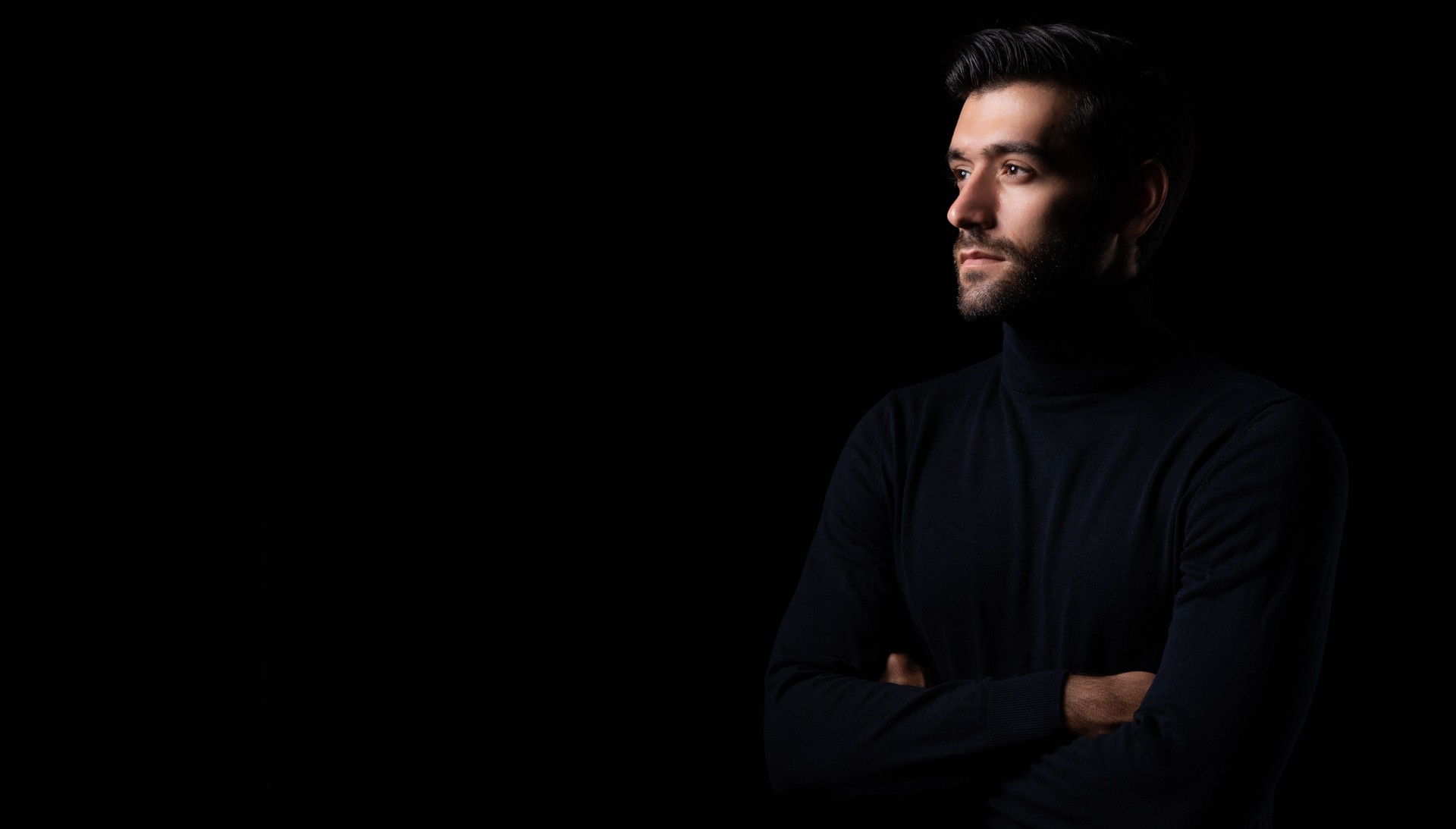 Confidence handsome young man with folded arms Attractive businessman look at copy space with crossed arms studio shot standing in the dark room black background Successful young guy portrait